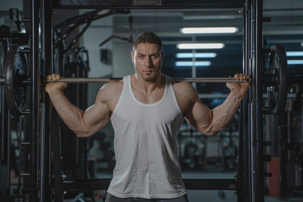 A strong, muscular man in a white tank top lifting weights in the gym.